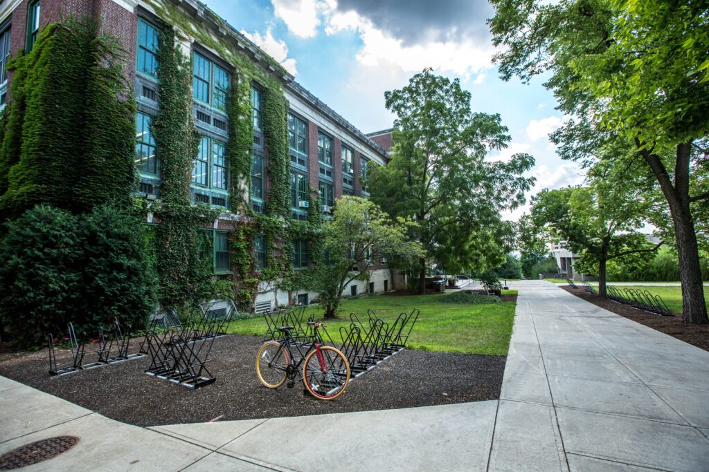 Partial vew of a university campus, with concrete walkways, brick buildings, one bicycle attached to a bike rack, and lots of greener.