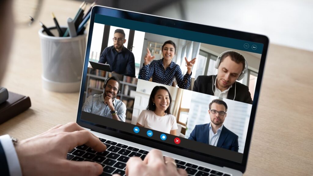 Laptop screen shows a video meeting with 6 participants, all visible on screen. The people are wearing business attire.