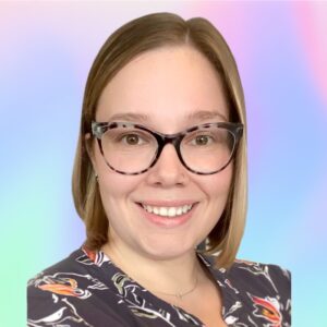 A person with short blond hair and glasses smiles at the camera. They are wearing a dark top with colorful patterns. The background is a soft gradient of pastel colors.